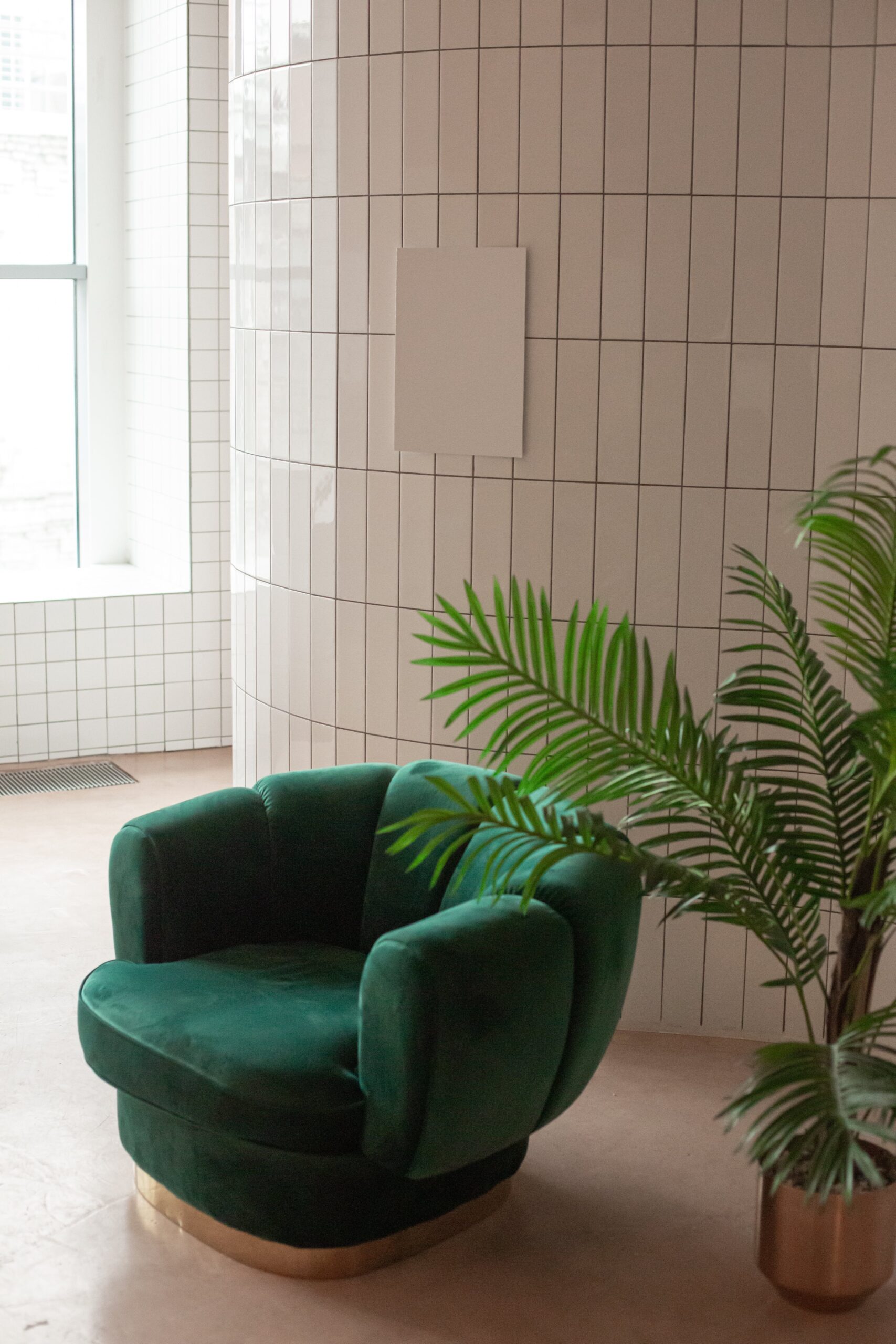 fauteuil en velours vert bouteille devant un mur en carreaux blanc et plante